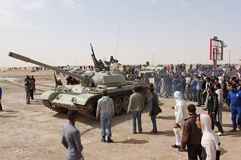 Armed rebels and civilian onlookers gathered at a main gateway into the eastern city of Ajdabiya to cheer on fighters heading onward to the fighting. Photo: al-Jazeera. Source: Wikimedia Commons.
